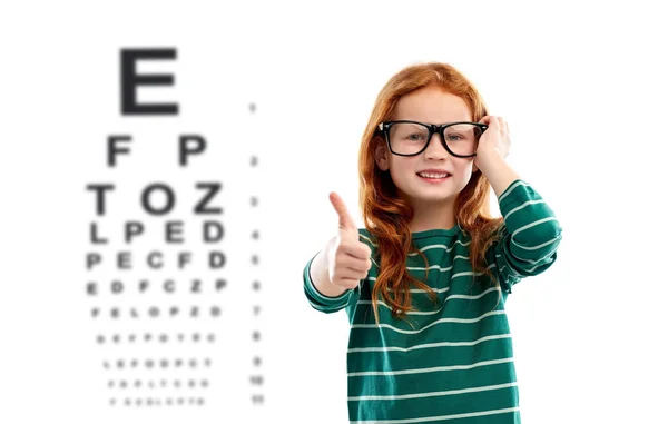 Fille aux cheveux rouges dans des lunettes sur le tableau de test oculaire — Photo