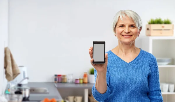 Donna anziana sorridente che mostra smartphone in cucina — Foto Stock