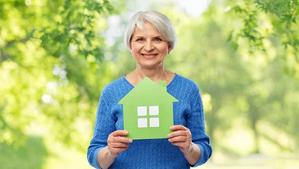 Усміхнена старша жінка тримає значок зеленого будинку — стокове фото