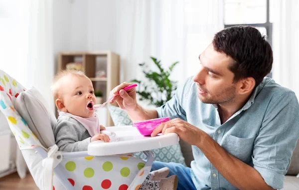 Father feeding happy baby in highchair at home — Stock Photo, Image