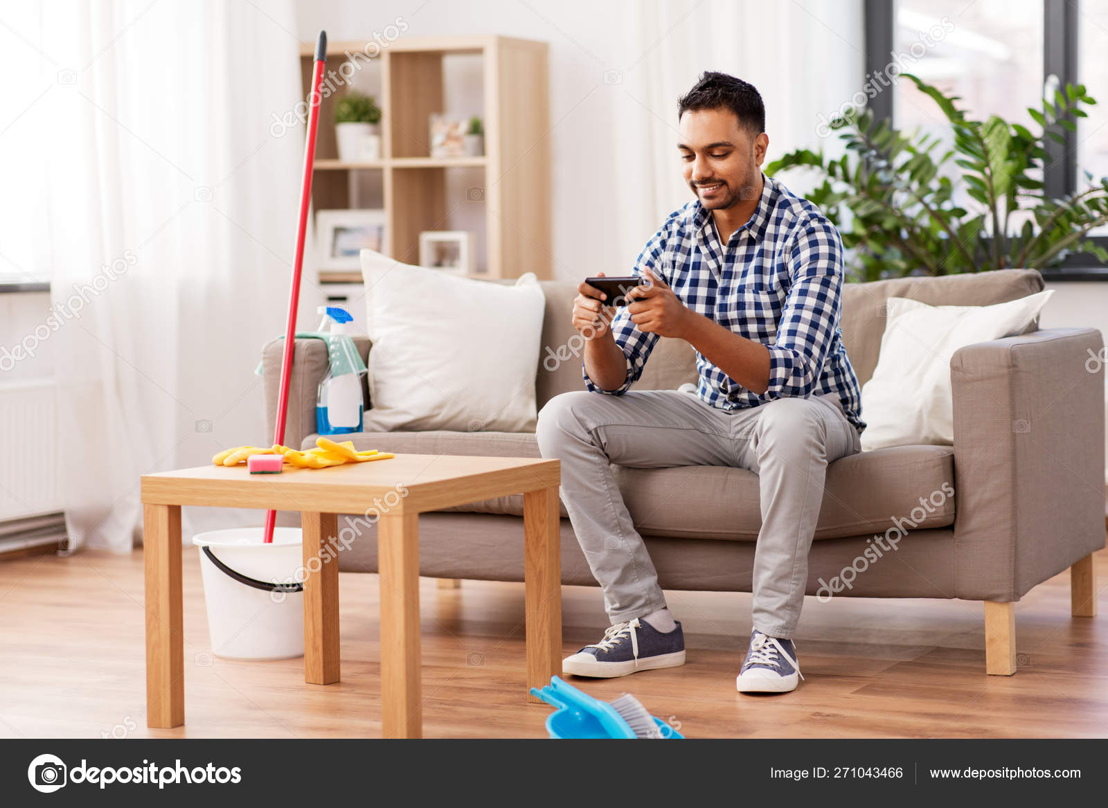 Man Playing Game On Smartphone After Cleaning Home