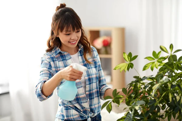 Happy asian woman spraying houseplant at home — Stock Photo, Image