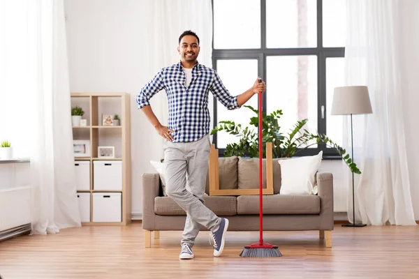 Sonriente indio hombre con escoba limpieza en casa — Foto de Stock