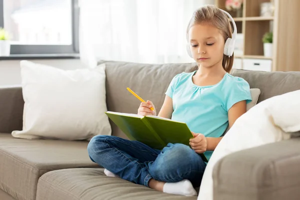 Dívka ve sluchátkách s deníkem na pohovce doma — Stock fotografie