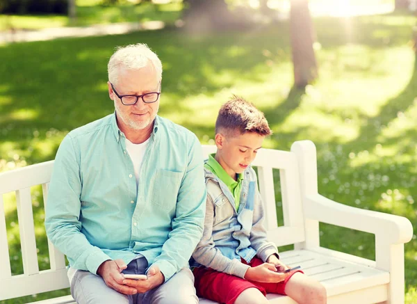 Hombre viejo y niño con teléfonos inteligentes en el parque de verano —  Fotos de Stock