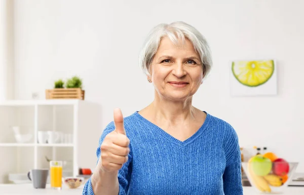 Lachende Senior vrouw die duimen omhoog in de keuken — Stockfoto