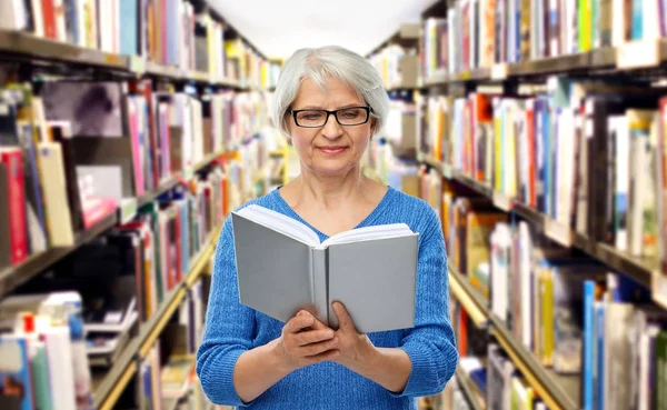 Mujer mayor en gafas libro de lectura en la biblioteca — Foto de Stock