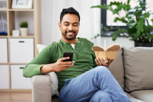 Hombre indio sonriente comiendo comida para llevar en casa — Foto de Stock