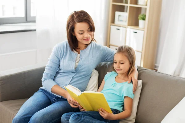 Счастливая девочка с мамой, читающей книгу дома — стоковое фото