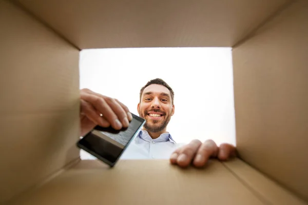 Smiling man taking smartphone out parcel box — Stock Photo, Image