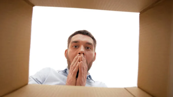 Шокований чоловік дивиться у відкриту коробку посилок — стокове фото