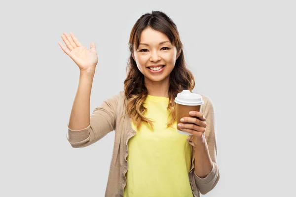 Feliz asiático mujer bebiendo café y saludando mano —  Fotos de Stock