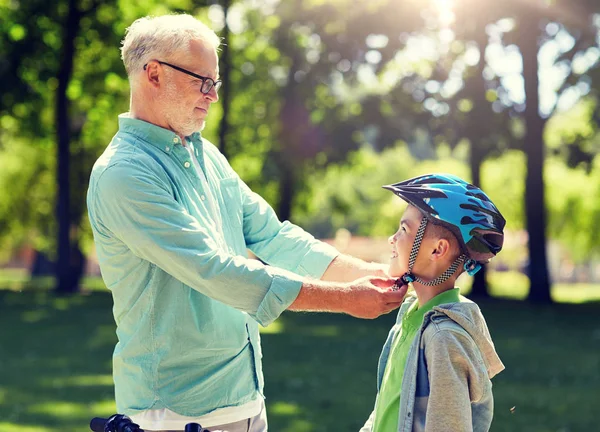 Anciano ayudando a niño con casco de bicicleta en el parque — Foto de Stock