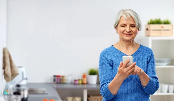 Uśmiechnięta kobieta senior za pomocą smartfona w kuchni — Zdjęcie stockowe