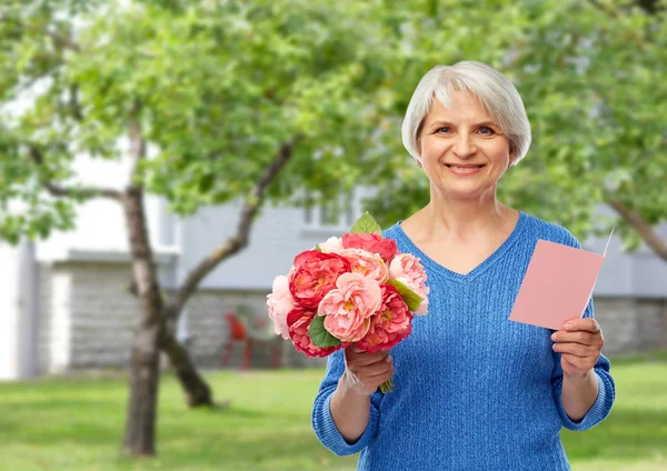 Gelukkige Senior vrouw met bloemen en wenskaart — Stockfoto