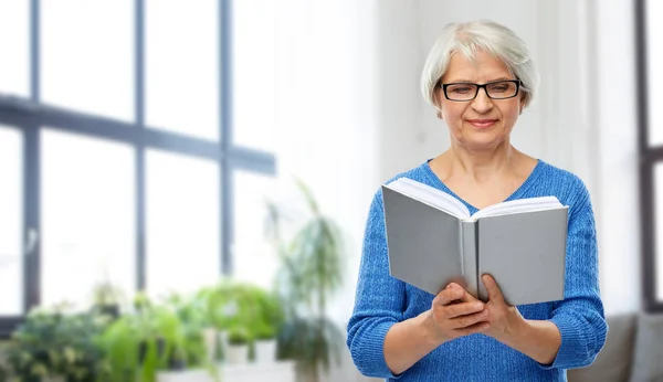 Wanita senior berkacamata membaca buku di rumah — Stok Foto