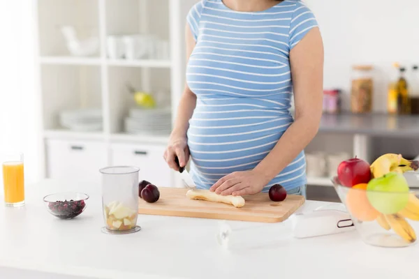 Mujer embarazada cortando frutas en la cocina casera —  Fotos de Stock