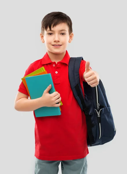 Chico con libros y la bolsa de la escuela mostrando pulgares hacia arriba —  Fotos de Stock