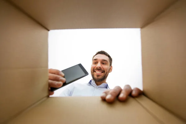 Lächelnder Mann holt Smartphone aus Paketkasten — Stockfoto