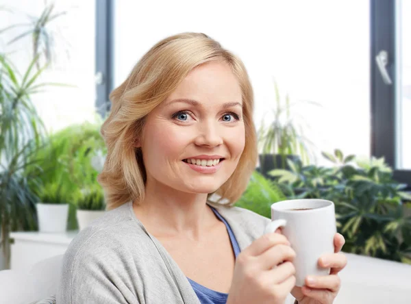 ผู้หญิงที่ยิ้มกับถ้วยชาหรือกาแฟที่บ้าน — ภาพถ่ายสต็อก