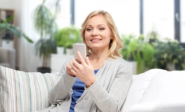Улыбающаяся женщина со смартфоном пишет смс дома — стоковое фото