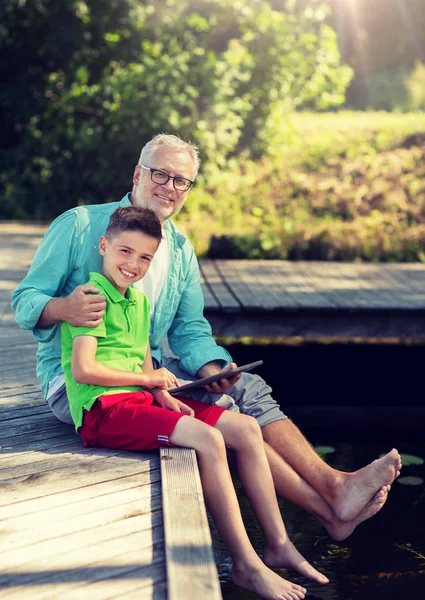 Großvater und Junge mit Tablet-PC auf Flussliegeplatz Stockbild