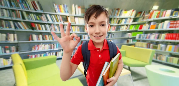 Elev pojke med böcker som visar OK på biblioteket — Stockfoto