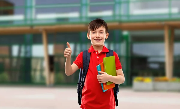 Estudiante chico con libros y bolsa mostrando pulgares hacia arriba — Foto de Stock