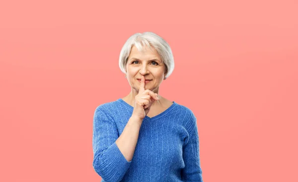 Mujer mayor haciendo gesto de silencio sobre rosa — Foto de Stock