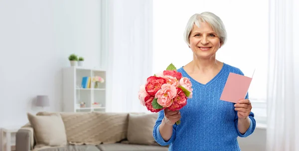 Mulher sênior feliz com flores e cartão de saudação — Fotografia de Stock