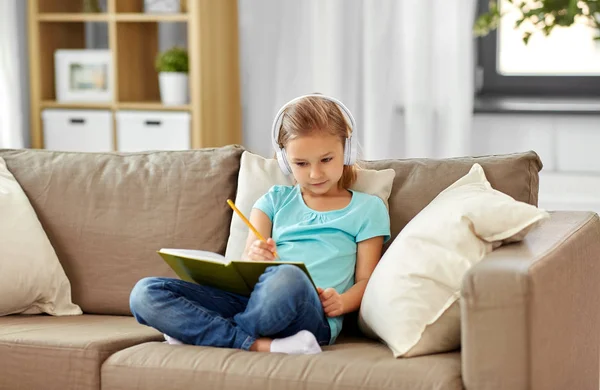 Ragazza in cuffia con diario sul divano di casa — Foto Stock