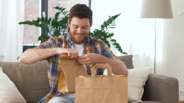 Hombre sonriente desempacando comida para llevar en casa — Vídeo de stock