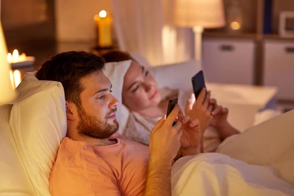 Pareja usando teléfonos inteligentes en la cama por la noche —  Fotos de Stock