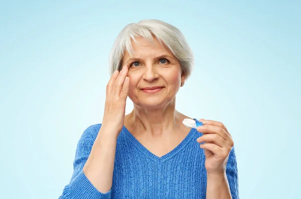 Mulher sênior aplicando lentes de contato sobre azul — Fotografia de Stock