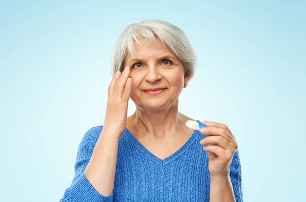 Mujer mayor aplicando lentes de contacto sobre azul — Foto de Stock