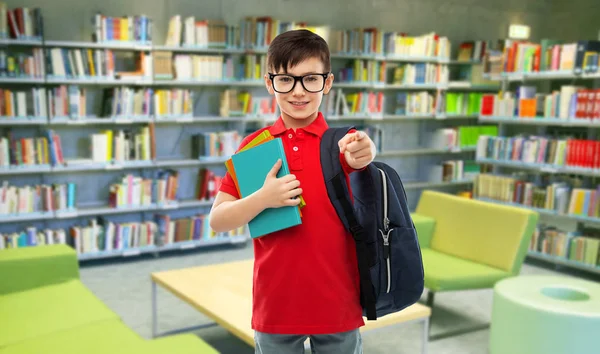 Улыбающийся школьник в очках с книгами в библиотеке — стоковое фото
