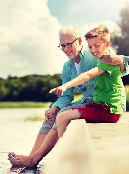 Дедушка и внук сидят на берегу реки — стоковое фото