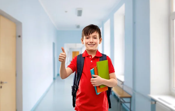 Estudiante chico con libros y bolsa mostrando pulgares hacia arriba — Foto de Stock