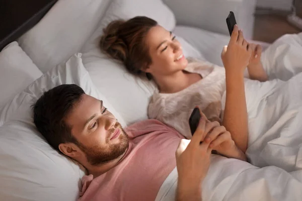 Pár pomocí chytrých telefonů v posteli v noci — Stock fotografie