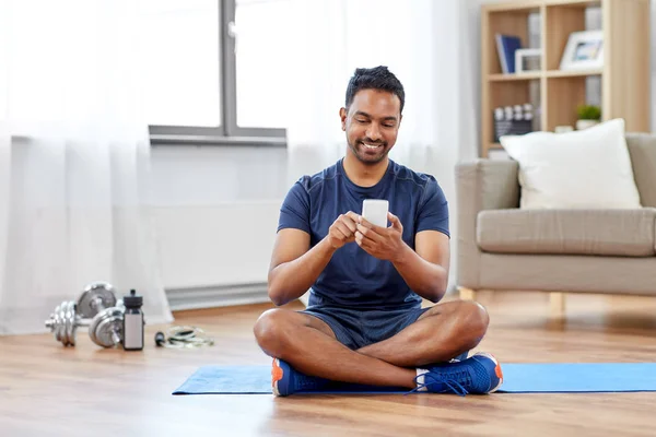 Hombre indio con teléfono inteligente en alfombra de ejercicio en casa —  Fotos de Stock