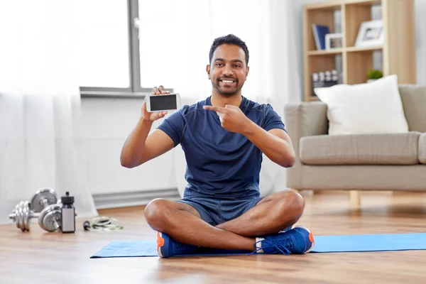 Homme indien avec smartphone sur tapis d'exercice à la maison Photo De Stock
