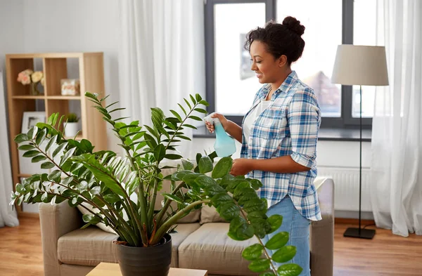 Donna felice spruzzando pianta d'appartamento con acqua a casa — Foto Stock