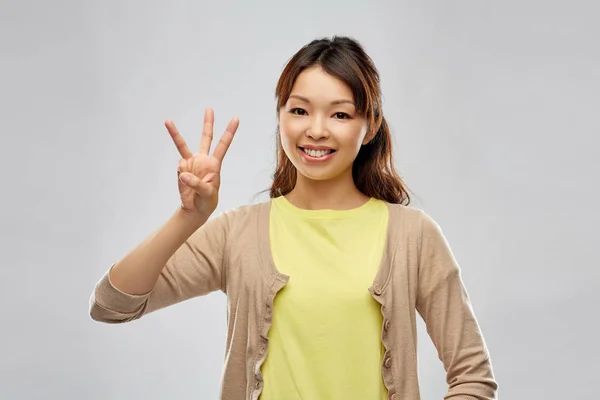 Sorrindo asiático mulher mostrando três dedos Imagens Royalty-Free