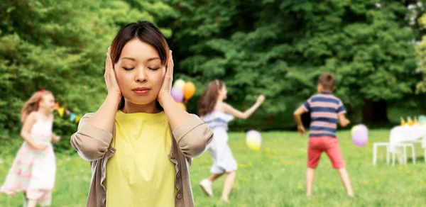 Asian woman closing ears over kids party at park — Stock Photo, Image