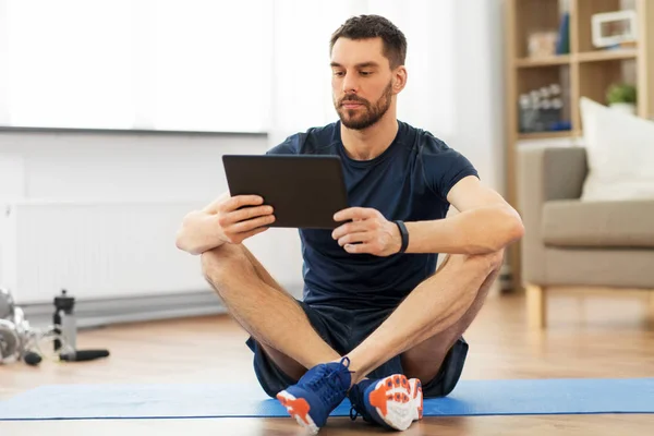 Homem com computador tablet no tapete de exercício em casa — Fotografia de Stock