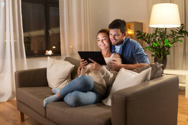 Szczęśliwa para przy użyciu komputera typu tablet w domu w godzinach wieczornych — Zdjęcie stockowe