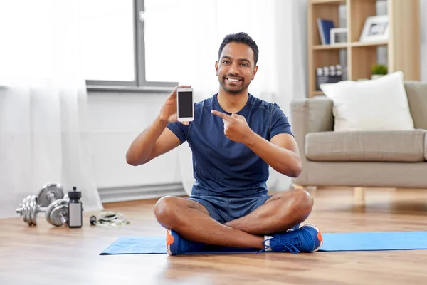 Hombre indio con teléfono inteligente en alfombra de ejercicio en casa —  Fotos de Stock