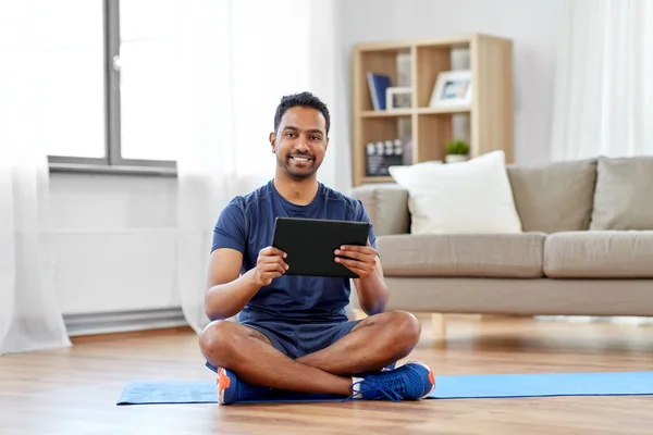 Homem indiano com tablet pc e tapete de exercício em casa Imagens De Bancos De Imagens