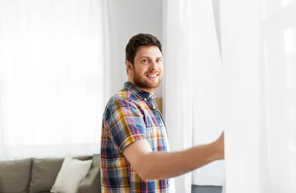 Joven hombre apertura ventana cortina en casa —  Fotos de Stock