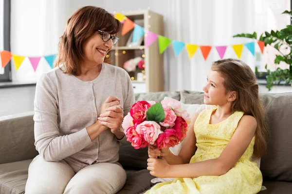 Granddaughter giving grandmother flowers at home — Stock Photo, Image